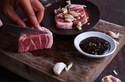 Cropped hands of woman cutting meat on cutting board