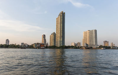 Modern buildings by river against sky in city