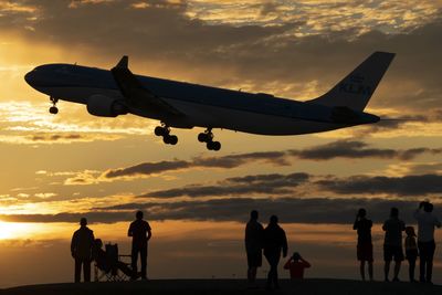 Silhouette people on airplane against sky during sunset