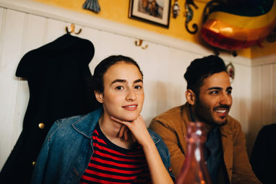 Portrait of smiling young woman sitting with hand on chin by man at restaurant during lunch party