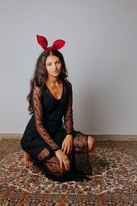 Portrait of beautiful young woman sitting against wall