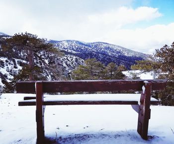 Bench in snow covered mountains against sky