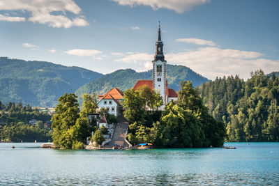 Scenic view of building by trees in lake by mountains against sky