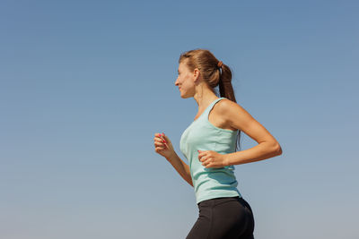Side view of young woman exercising against clear sky