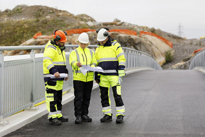 Engineers in reflective clothing looking at plans on bridge