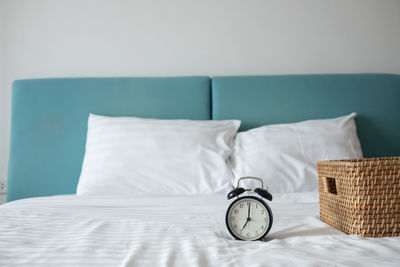 Clock by wicker basket on bed at home