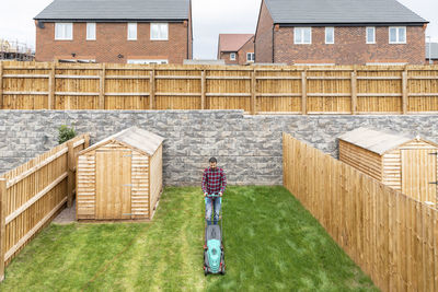 Man walking while using lawn mower at backyard against house