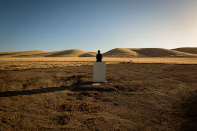 Rear view of man standing in desert against clear sky