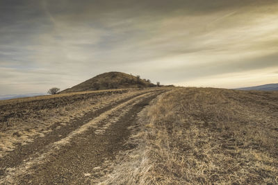 Panoramic view of a burial mound in a filed near a country road with cloudy skies in the background