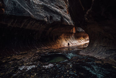 Silhouette woman walking by rock formation in cave