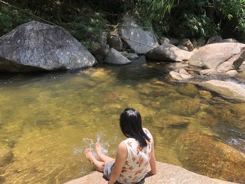 Rear view of woman sitting on rock by lake