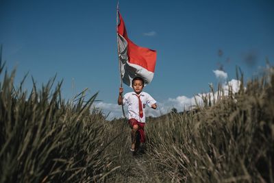 Portrait of boy standing on field against sky