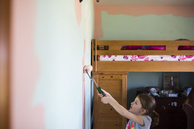 Side view of girl painting wall at home