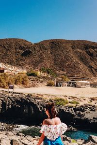 Rear view of woman looking at mountain against clear sky