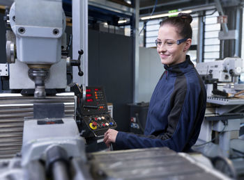 Smiling engineer with protective glasses operating cnc machine at factory