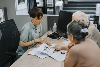 Senior couple discussing with female interior designer over brochure at desk in store