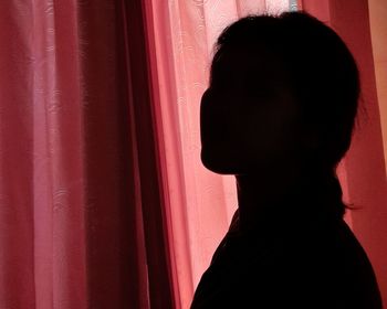 Close-up portrait of silhouette woman standing against red wall