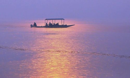 Silhouette people on sea against sky during sunset