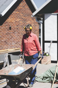 Senior woman pushing wheelbarrow at yard outside house