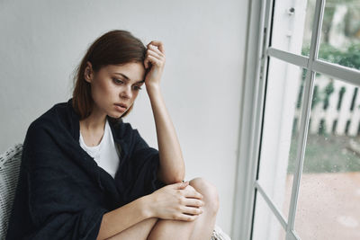 Portrait of a young woman sitting against window