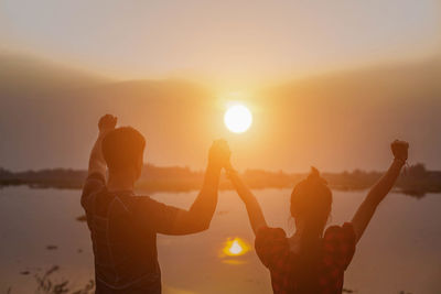 Silhouette people with arms raised standing against sky during sunset