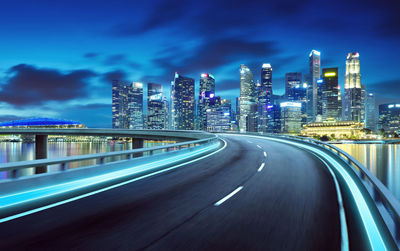 Illuminated bridge by buildings against sky at night