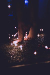 Low section of woman standing by fairy lights on road at night