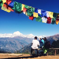 Rear view of people sitting on bench by himalayas against sky