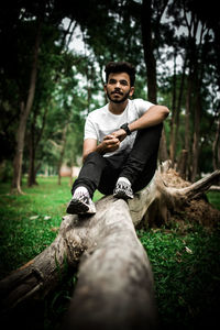 Portrait of young man sitting on tree trunk