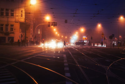 Railroad tracks on street in illuminated city at night