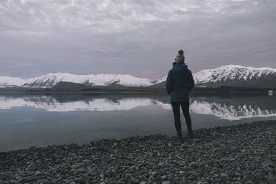 Young woman on a blue jacket standing in front of lake tekapo, nz