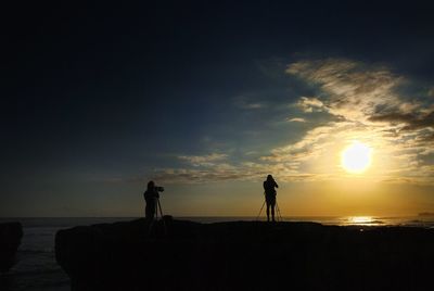 Silhouette of people standing on beach at sunset