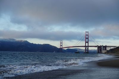 Suspension golden gate bridge over river against cloudy sky