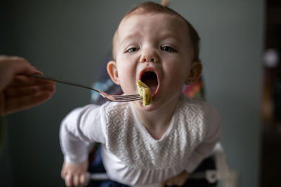 Cropped hand of mother feeding food to cute daughter with fork at home