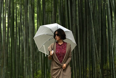 View of a woman holding a white umbrella in the bamboo forest