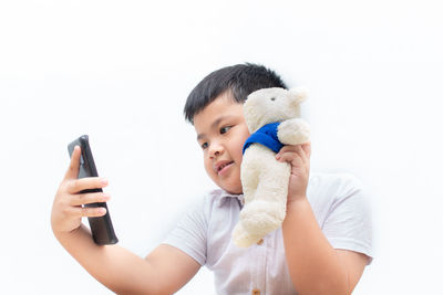 Boy holding toy while standing against white background