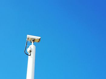 Low angle view of security camera against clear blue sky