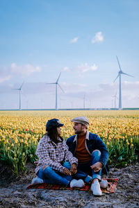 People relaxing on field against sky