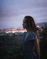 Side view of young woman standing against sky