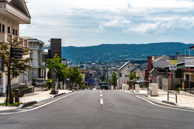 Road by buildings in city against sky