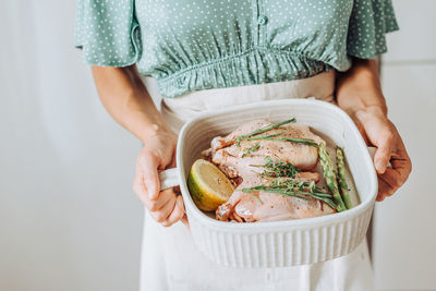 Close up hands holding a tray with raw quail and aromatic herbs