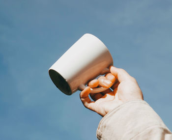 Low angle view of person holding cup camera against sky