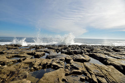 Panoramic view of waves splashing on sea against sky