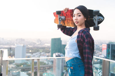 Portrait of young woman standing against railing in city