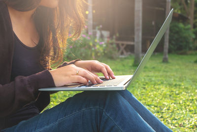 Midsection of woman using laptop on field