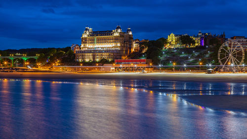 Buildings by river against sky at night