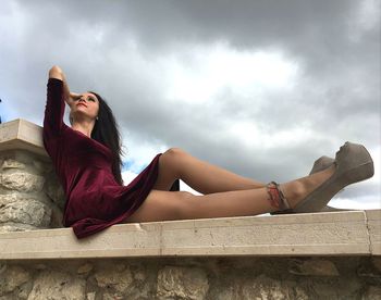 Woman sitting on roof against cloudy sky