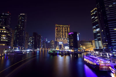 Illuminated buildings by river against sky in city at night