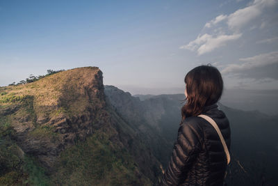 Woman looking at mountain while standing against sky