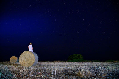 Rear view of young woman sitting on hay bale against star field